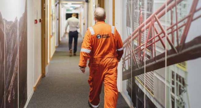A worker dressed in an orange overall is walking in a corridor