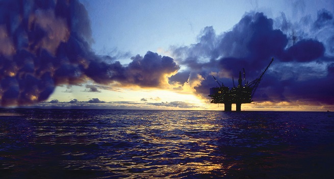 Wide shot of the sea at sunrise, showing the silhouette of an oil rig